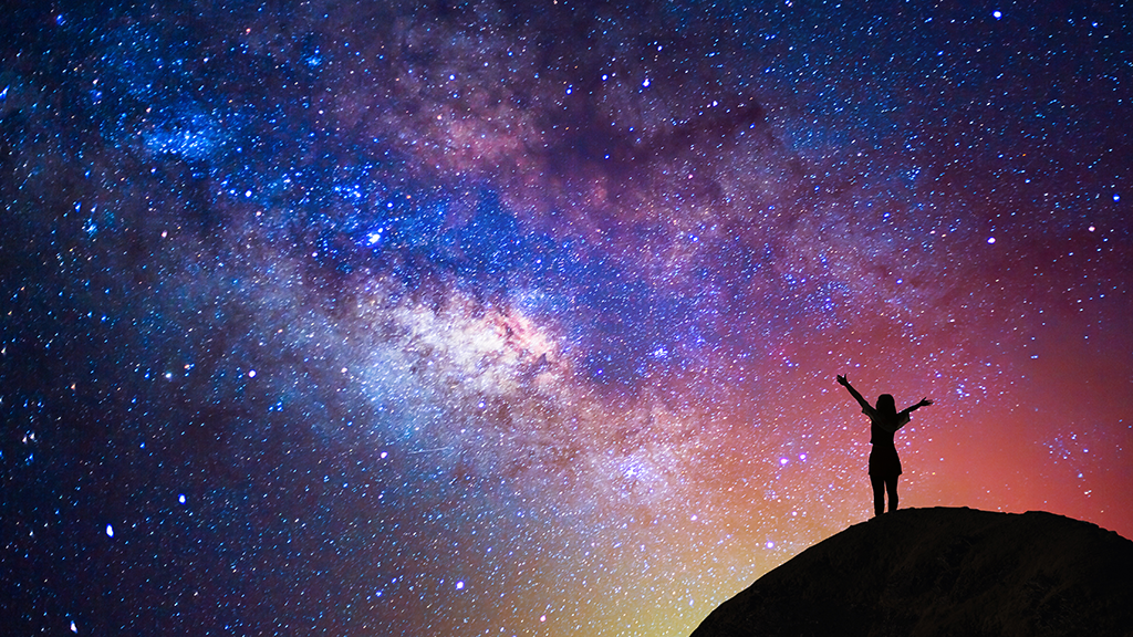 A person with his arms wide open looking at the sky at night